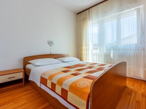 A bedroom with a wooden bed, white bedding, a patterned throw blanket, a nightstand, and a window with sheer curtains. - Appartement für 3 Personen mit Balkon by Interhome (Crikvenica)