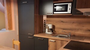 Cocina compacta con microondas, cafetera y pileta. Incluye una mesa de madera y una silla.