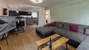 Una sala de estar moderna con un sofá gris, una mesa de centro de madera y un comedor con una mesa y sillas negras.