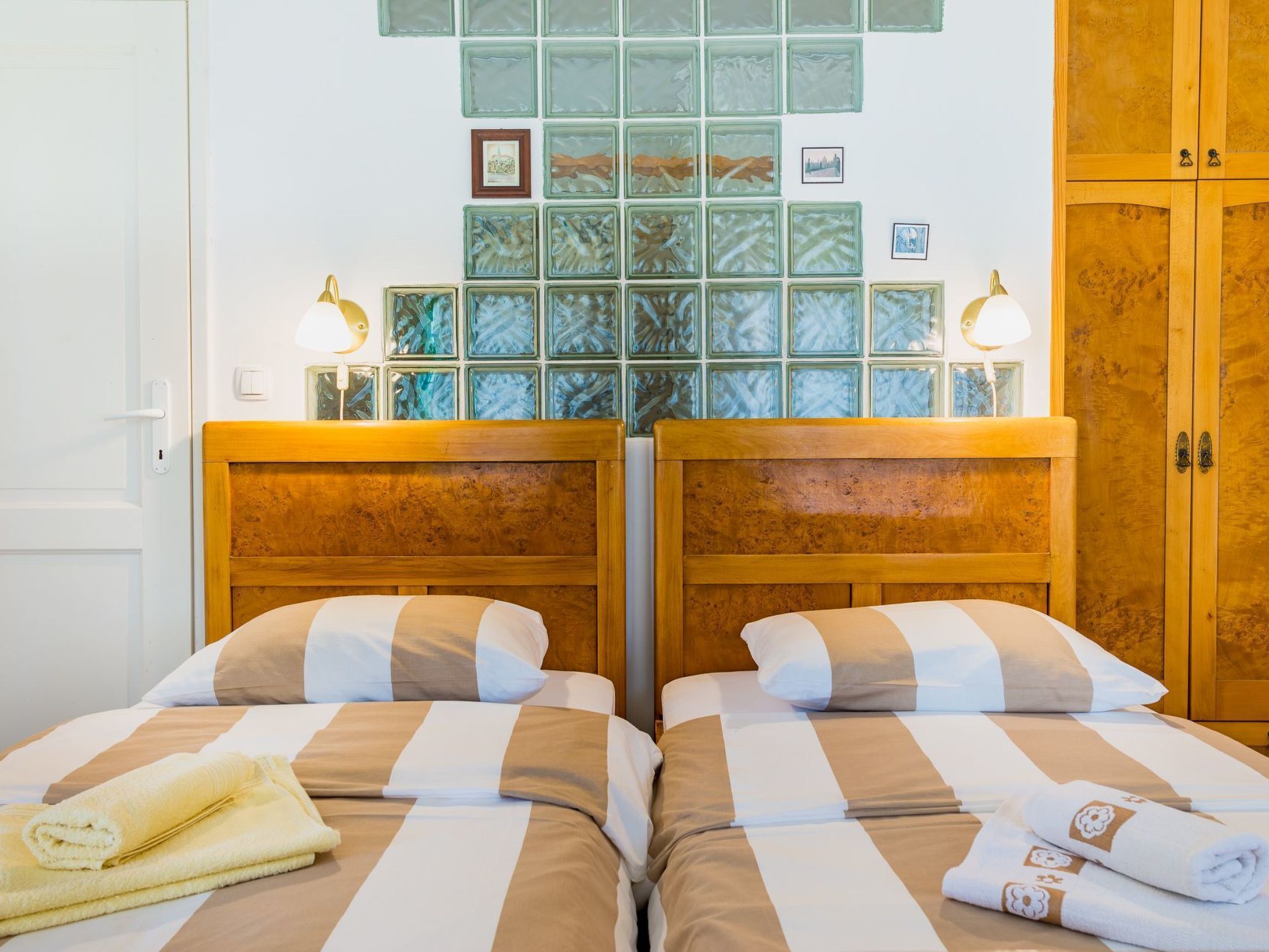 Habitación de hotel con dos camas, cabecera de madera, pared con cuadros enmarcados y un armario.