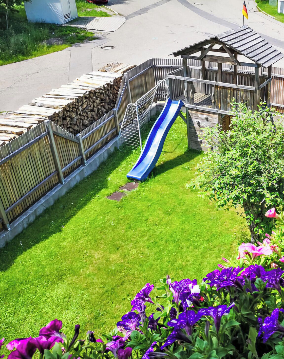 Ein Spielplatz mit Rutsche, einem eingezäunten Bereich und einer kleinen Gebäudestruktur.