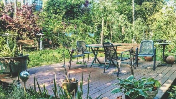 Une terrasse extérieure dotée d’une plateforme en bois, de chaises et de tables en métal, le tout entouré d’une végétation luxuriante et de plantes en pot.