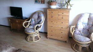 Un salon avec deux fauteuils en osier, un meuble en bois, un téléviseur et un élément décoratif mural.