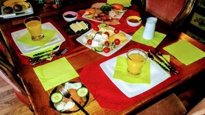 A wooden dining table with various food items and drinks, including plates of cheese, vegetables, and a glass of juice. - Ferien-Apartment  1 by Interhome (Blankenheim)