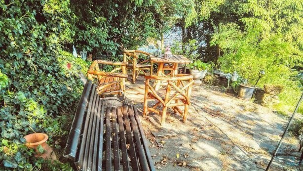 A rustic outdoor seating area with wooden furniture and a bench, surrounded by lush greenery. - Ferien-Apartment  1 by Interhome (Blankenheim)