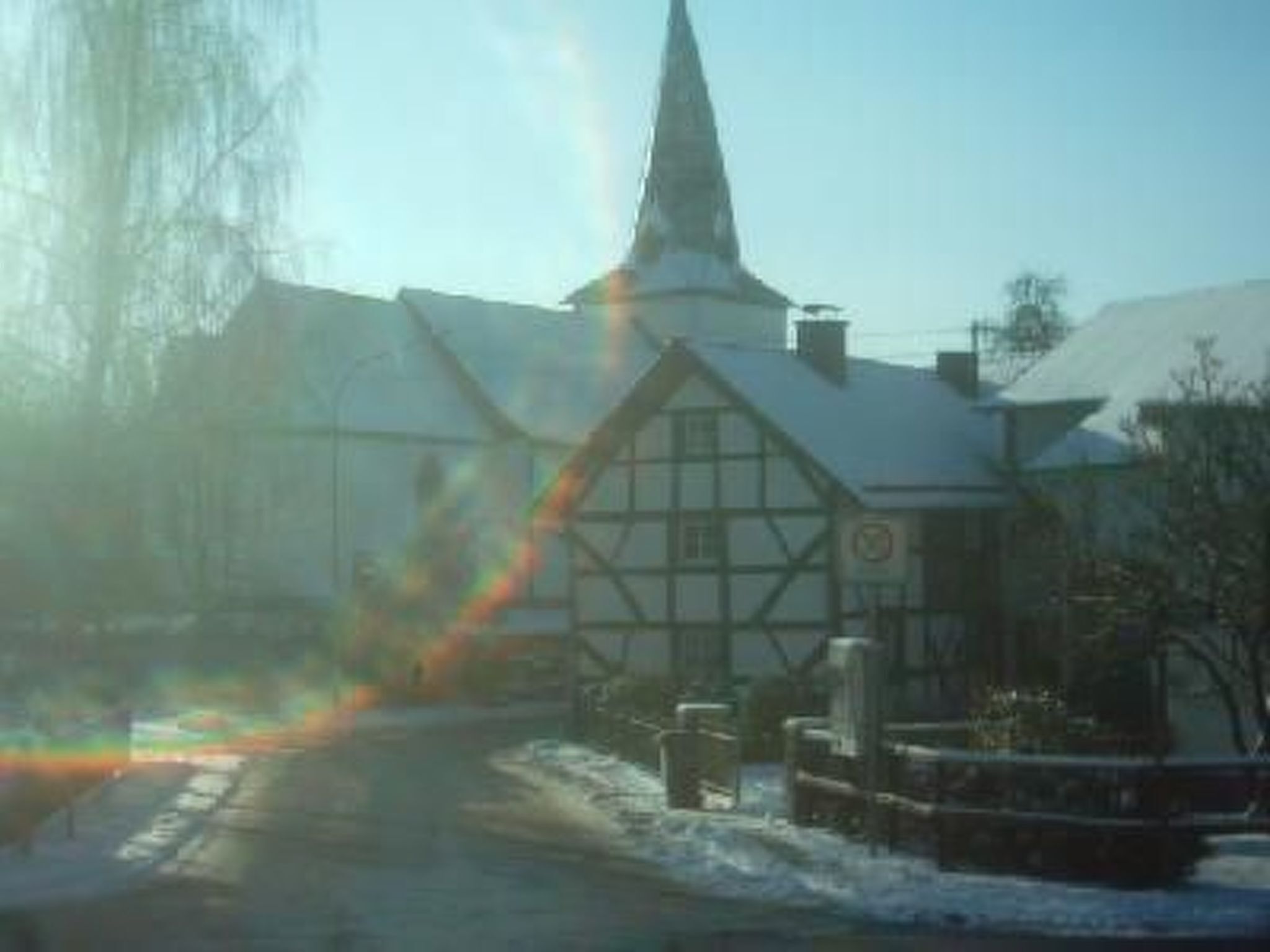 A traditional half-timbered building with a steeply pitched roof and a prominent tower, likely a church or chapel, in a snowy setting.