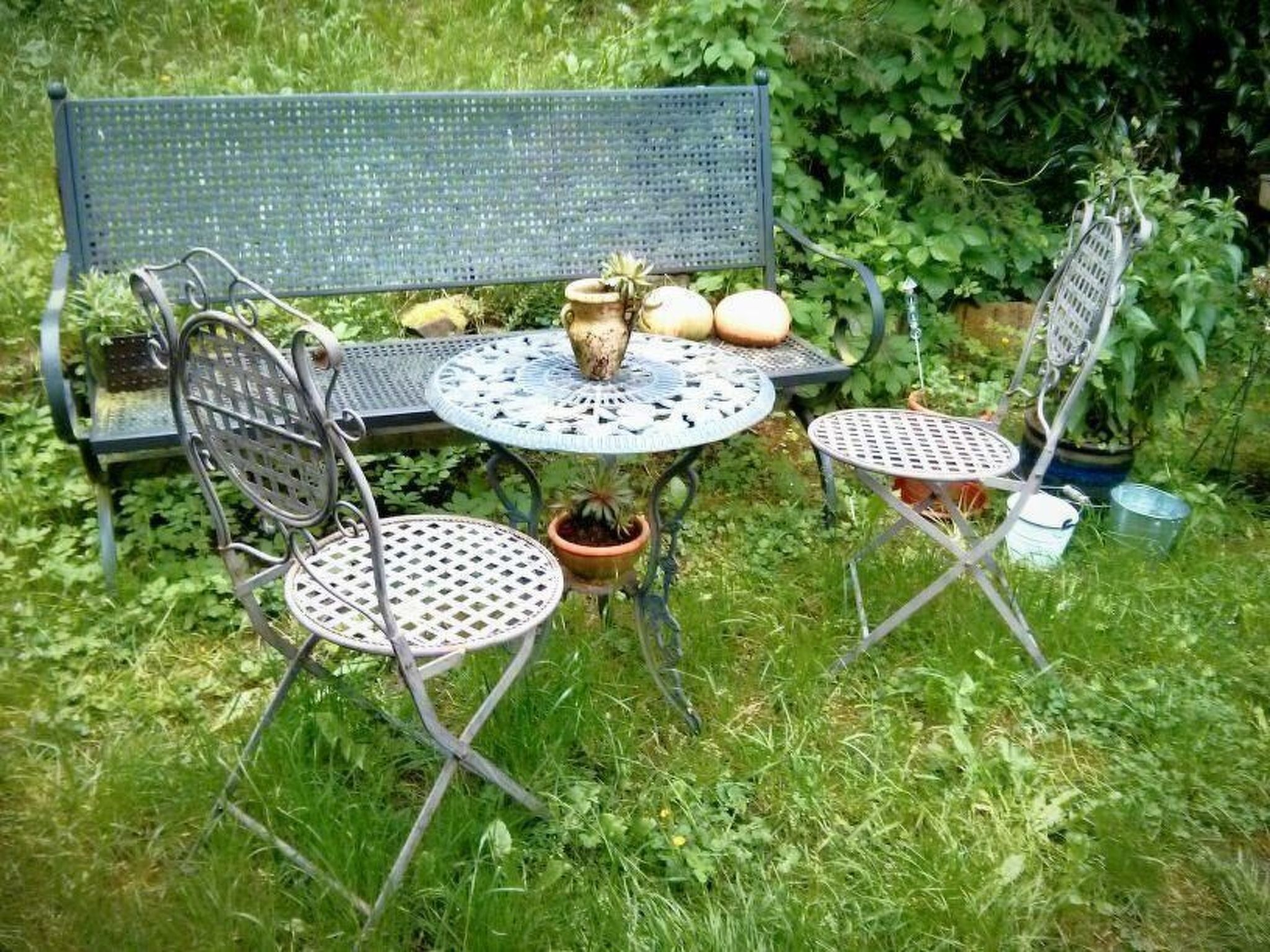 A garden setting with a metal bench, two metal tables, and potted plants.