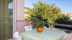 En balkon med et bord, stole, en potteplante og udsigt til træer og bygninger.