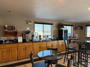 A kitchen with wooden cabinets, a microwave, a coffee machine, and a glass table with chairs. - Cassville Four seasons inn & suits (Cassville)
