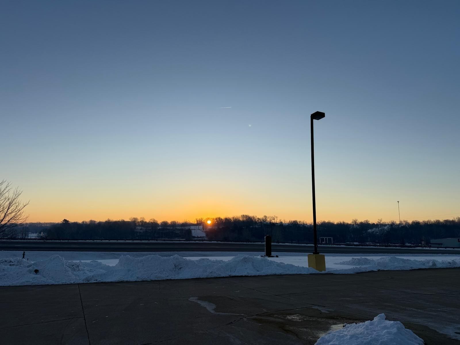 A parking lot with snowbanks and a street lamp.