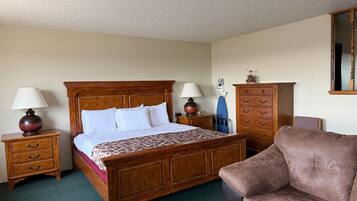 Une chambre d’hôtel avec un lit en bois, deux tables de chevet avec des lampes, une commode en bois, un canapé en cuir marron et un miroir au mur.
