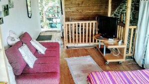 Une pièce chaleureuse avec un canapé rouge, un petit téléviseur posé sur un meuble en bois et un lit recouvert d’une couverture à rayures.