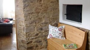 A room with a stone wall, a wooden bench with a floral cushion, and a mounted television. - Little Stonehouse by Interhome (Blankenheim)