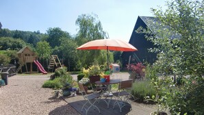 A wooden deck with a table and chairs, surrounded by potted plants and a playground. - Little Stonehouse by Interhome (Blankenheim)