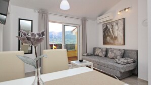 Ein modernes Wohnzimmer mit einer Couch, einem Esstisch mit einer Vase und einem großen Fenster mit Blick auf die Berge.