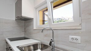 Eine moderne Küche mit zwei Edelstahl-Spülen, einem Fenster mit Blick auf Grünflächen und einer weißen, gefliesten Spritzschutzwand.