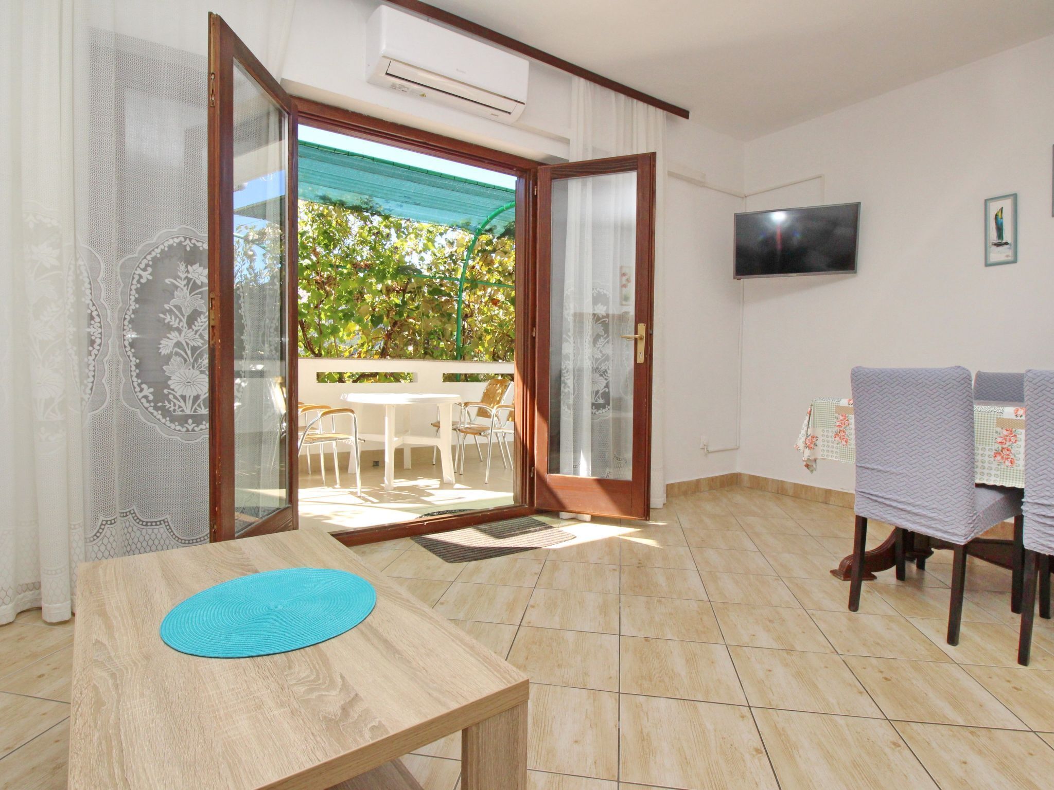 A room with a wooden table, a TV mounted on the wall, and a sliding glass door leading to an outdoor area with a table and chairs.