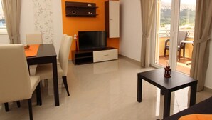 Un saló modern amb televisió plana, taula de dinar amb caires, taula auxiliar petita i un balcó amb vistes.