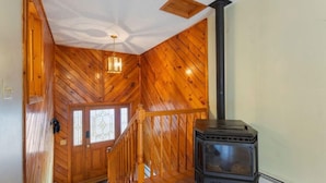 A wooden interior with a staircase, a wood-paneled wall, and a black wood-burning stove. - Walk to the slopes from this BMOM 3 bedroom. (Rumford)