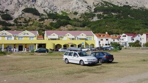 Una hilera de edificios amarillo y blanco con un área de estacionamiento al frente, con montañas al fondo.