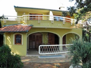 Una villa amarilla con el nombre "Villa Stefany" en la fachada, que cuenta con un porche cubierto y un balcón.