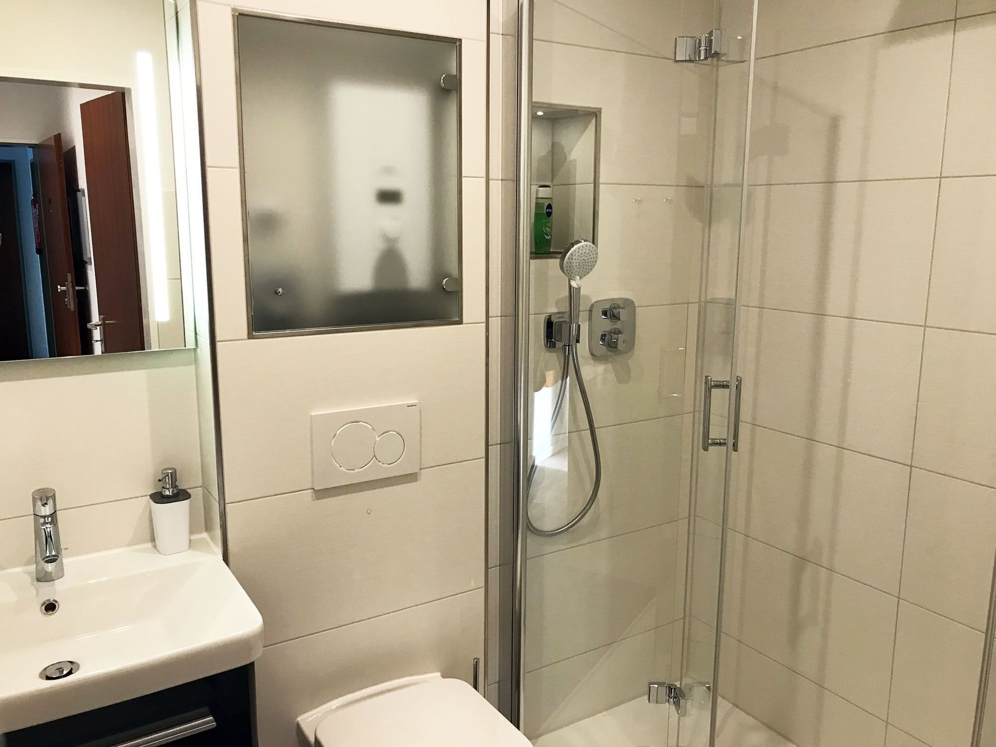 Een moderne badkamer met een douchecabine van glas, een wastafel met spiegel en een toilet.