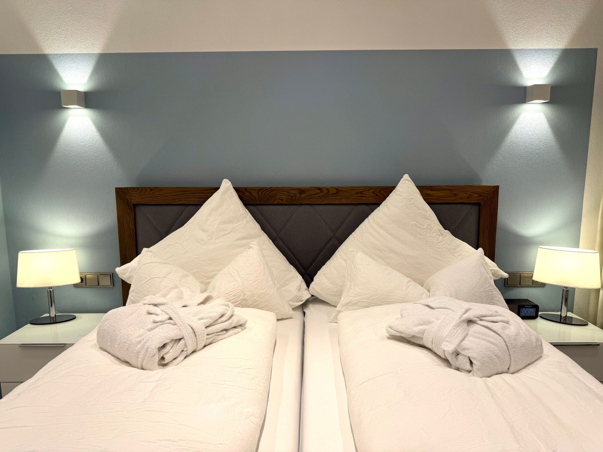 Ett hotellrum med två sängar, var och en med vita sängkläder och kuddar, ett träfärgat sänggavel och sänglampor.