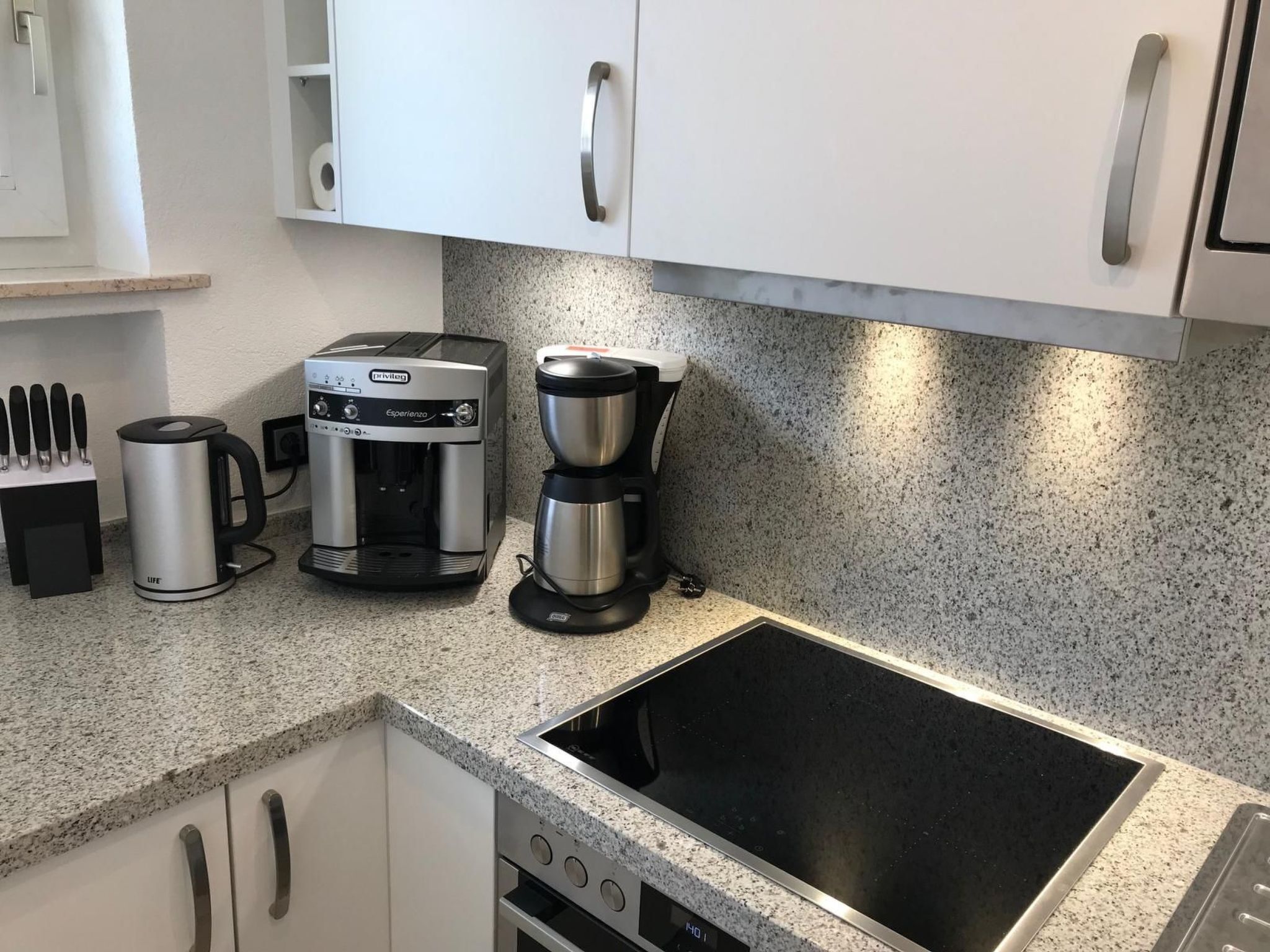 A kitchen with white cabinets, a granite countertop, a coffee maker, a toaster, and a stove.