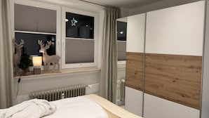 Ein Schlafzimmer mit einem Bett, einem Heizkörper, einem Fenster mit Jalousien und einem Kleiderschrank.
