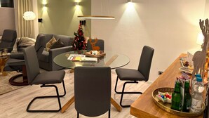 Ein modernes Wohnzimmer mit einem runden Glastisch, grauen Sofas und einem Holzesstisch mit Stühlen. Ein Weihnachtsbaum und eine Rentier-Dekoration sind sichtbar.