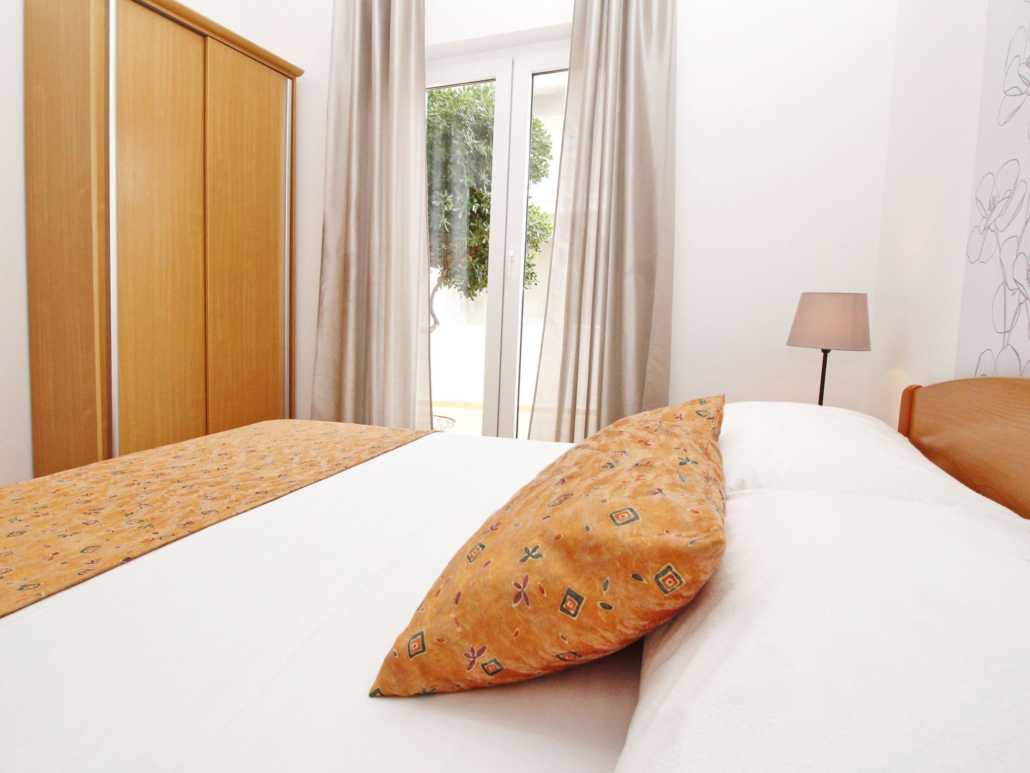 A hotel room with a bed, a nightstand, a lamp, and a view of greenery outside.