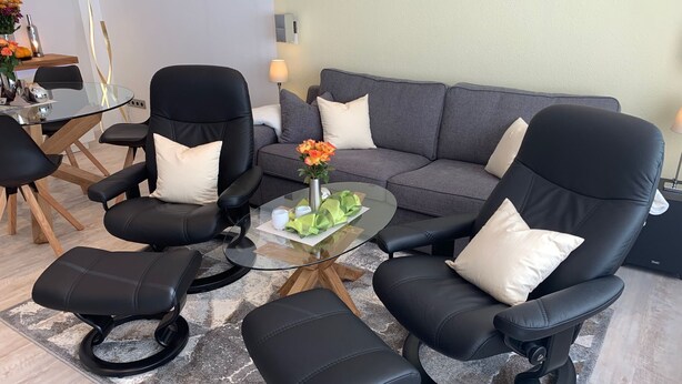 Un salon moderne avec un canapé gris, des fauteuils en cuir noir et une table basse en verre.