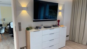 Un salon moderne avec un téléviseur à écran plat fixé au mur, un meuble blanc avec des tiroirs et une petite plante posée sur le meuble.