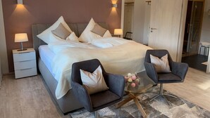 Une chambre moderne avec un grand lit, deux tables de chevet, une table basse en verre et deux fauteuils.