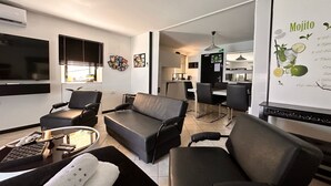 Un salon moderne comprenant un canapé, des fauteuils, une table basse et un téléviseur. Il y a également un coin repas avec une table et des chaises.