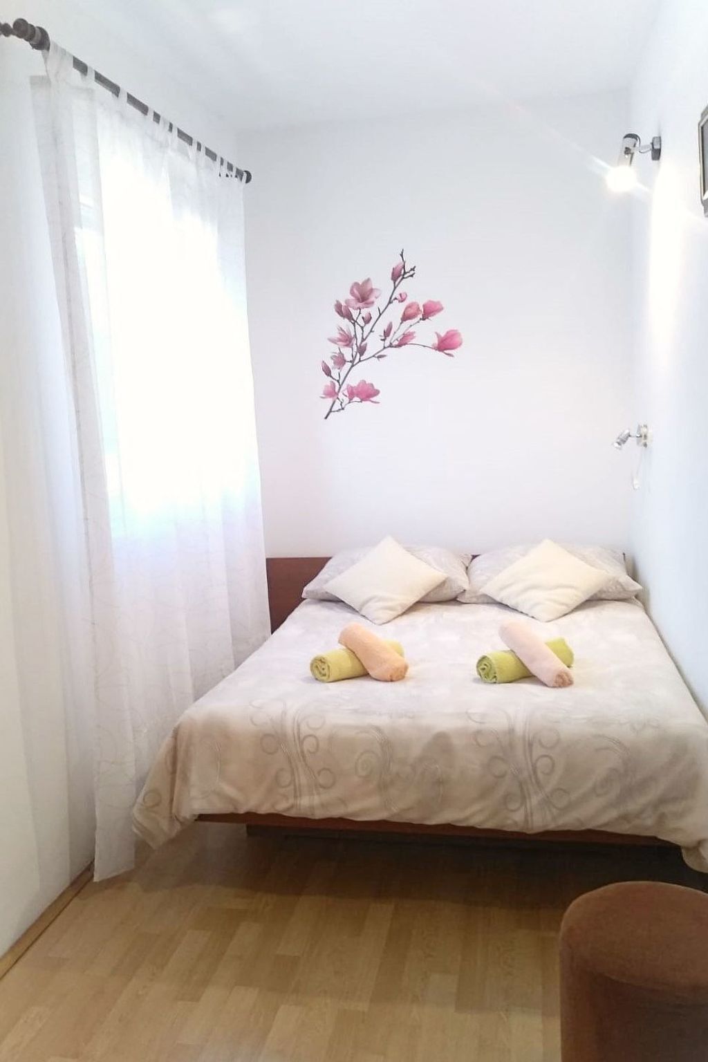 A small, neatly made bed with a patterned bedspread, two pillows, and rolled towels on the side.