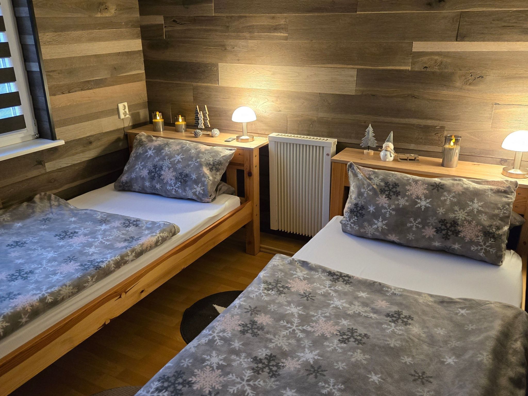 Une pièce confortable avec deux lits en bois, une petite table, un radiateur et une fenêtre avec des stores.