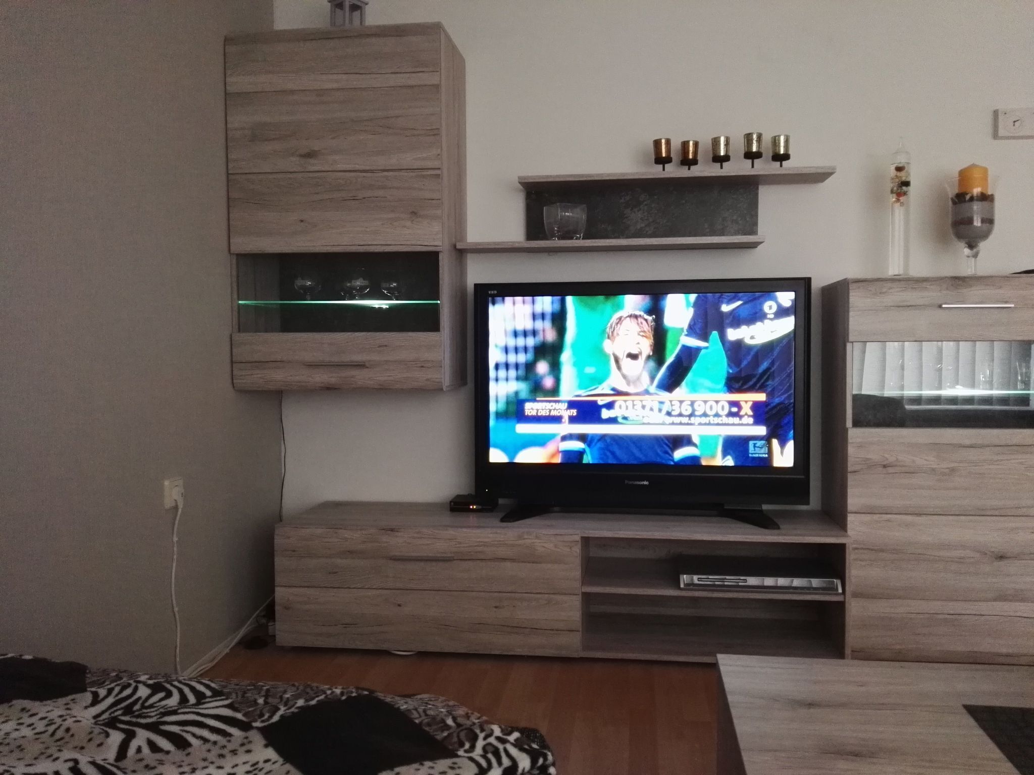 Una sala de estar con un televisor sobre un mueble de madera, un estante con objetos decorativos y un aparador de vidrio.