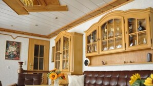 Een woonkamer met een bruine leren bank, een houten tafel met een vaas zonnebloemen, en houten kasten met glazen deuren.