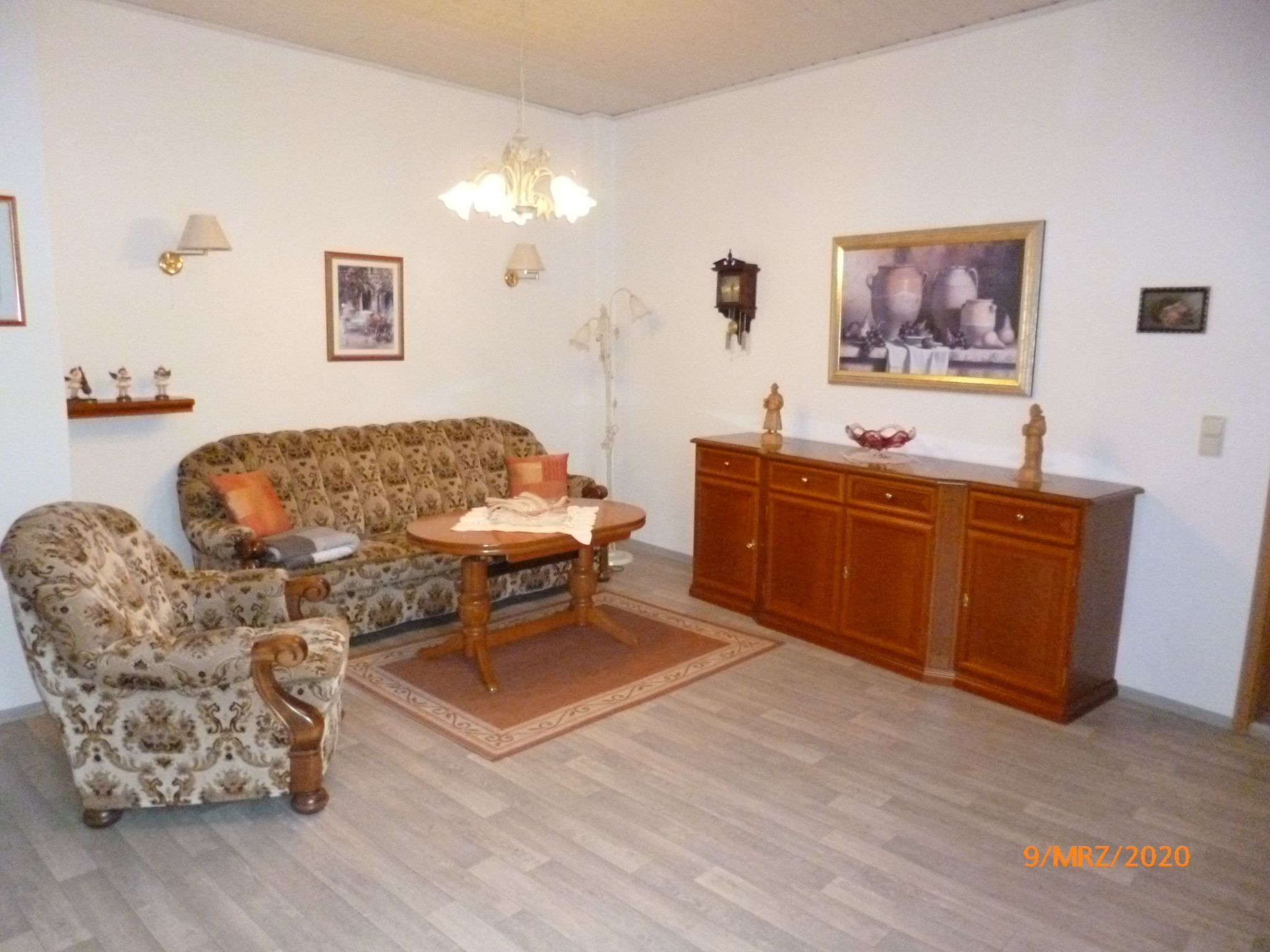 Una sala de estar con sofá, sillón, aparador de madera y candelabro.