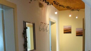 Un couloir doté d’un plancher en bois, une petite table sur laquelle est posée une plante en pot, un miroir et des crochets fixés au mur.