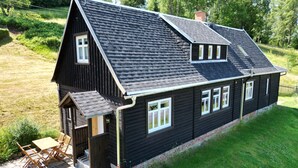 A two-story wooden house with a sloped roof, a front porch with a table and chairs, and a brick foundation. - Anno Dazumal by Interhome (Klingenthal)