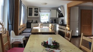 Une cuisine chaleureuse avec des poutres en bois, une table à manger avec des chaises et une vue sur l’extérieur.