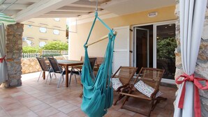 Un espacio patio con una hamaca colgante, sillas de madera, una mesa y un muro de piedra.