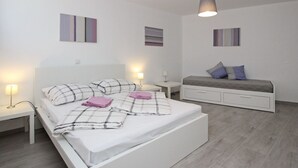 A modern bedroom with a white bed, bedside tables, a dresser, and abstract wall art. - Wohnung in Baška mit Terrasse by Interhome (Krk/Baška)