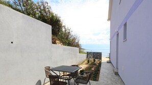 An outdoor patio with a table and chairs, a white wall, and a view of the sea. - Wohnung in Baška mit Terrasse by Interhome (Krk/Baška)