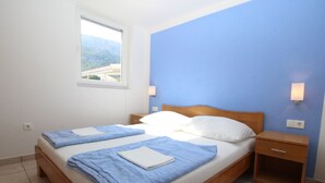 Una cama doble con ropa de cama azul, un cabecero de madera, una mesita de noche y una lámpara de pared.