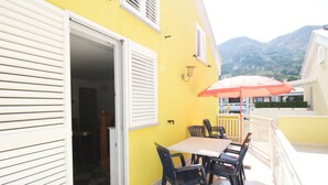 Edificio amarillo con un patio que incluye una mesa, sillas y una sombrilla roja, con vistas a montañas.