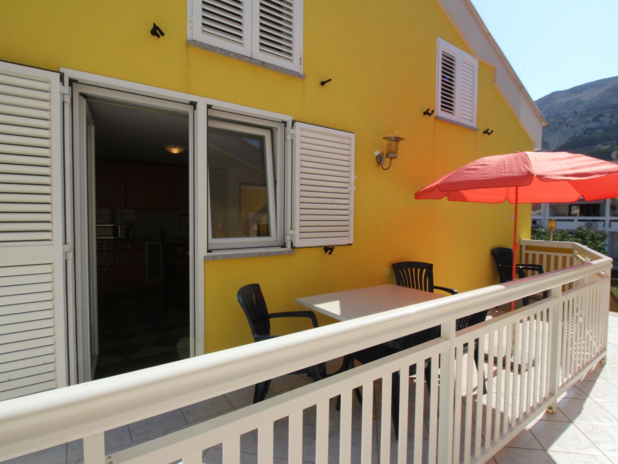 A yellow building with a balcony, white shutters, and a red umbrella.