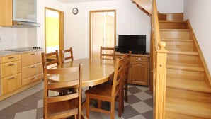 Cocina compacta con armarios de madera, una mesa de comedor con sillas, televisor integrado y una escalera.
